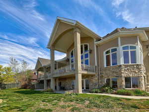 Rear view of house featuring a patio area, a balcony, a lawn, stone siding, and cooling unit