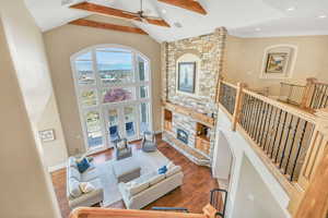 Living area featuring high vaulted ceiling, ceiling fan, wood finished floors, and a stone fireplace