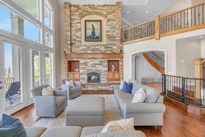 Living area featuring recessed lighting, wood finished floors, a high ceiling, stairway, and a stone fireplace