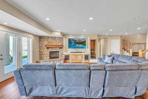 Living area with stairway, a stone fireplace, wood finished floors, arched walkways, and recessed lighting