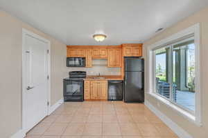 Kitchen featuring a sink, baseboards, black appliances, light countertops, and light tile patterned floors