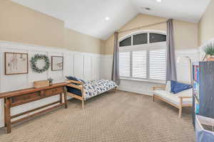 Bedroom with a decorative wall, wainscoting, carpet floors, lofted ceiling, and visible vents