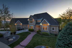 Craftsman-style house with stone siding, a front lawn, fence, and a shingled roof