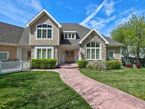 View of front facade featuring a front lawn, fence, stone siding, and roof with shingles