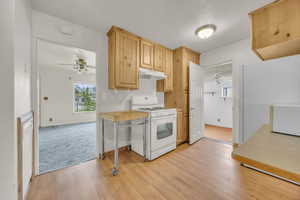 Kitchen with under cabinet range hood, a ceiling fan, light brown cabinetry, and gas range gas stove