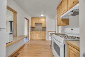 Kitchen featuring light brown cabinets, under cabinet range hood, light wood-style floors, and white appliances