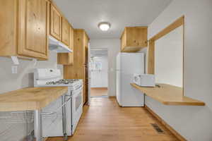 Kitchen with light wood-style flooring, visible vents, a ceiling fan, white appliances, and under cabinet range hood