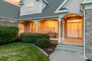 Doorway to property with brick siding, a porch, and a shingled roof