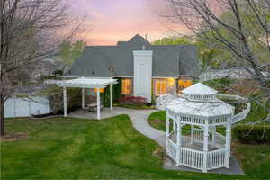 Rear view of property featuring a pergola, fence, a patio area, a lawn, and a shingled roof