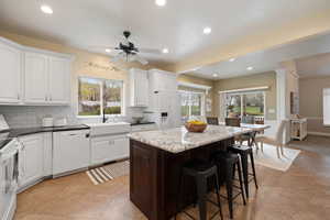 Kitchen with a sink, backsplash, white appliances, a breakfast bar, and a kitchen island
