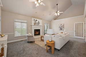 Carpeted living room featuring plenty of natural light, a warm lit fireplace, ceiling fan, and high vaulted ceiling