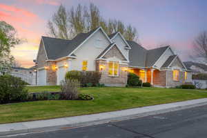 View of front facade featuring an attached garage, stone siding, a front yard, and stucco siding