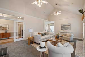 Carpeted living area featuring high vaulted ceiling, ceiling fan, and french doors
