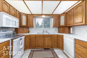 Kitchen featuring a sink, light countertops, white appliances, brown cabinets, and light floors