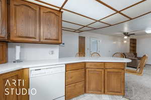 Kitchen featuring brown cabinetry, a peninsula, light countertops, and white dishwasher