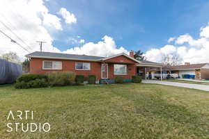Ranch-style home with a carport, a front yard, brick siding, a chimney, and concrete driveway