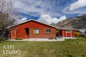 Rear view of property with a mountain view, brick siding, a patio area, and a lawn
