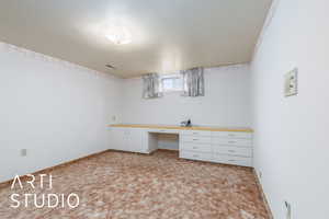 Basement with baseboards, light carpet, built in study area, and visible vents