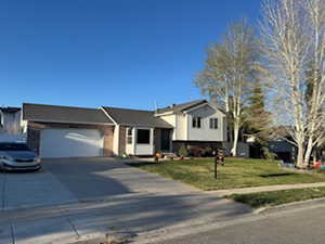 Split level home featuring concrete driveway, an attached garage, a front yard, brick siding, and a shingled roof
