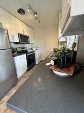 Kitchen with dark countertops, washer / dryer, rail lighting, appliances with stainless steel finishes, and visible vents