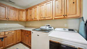 Washroom with a textured ceiling, washing machine and dryer, visible vents, cabinet space, and light tile patterned floors
