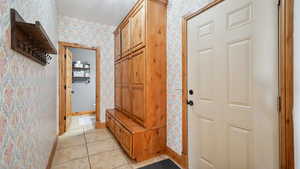 Mudroom with wallpapered walls, a textured ceiling, baseboards, and light tile patterned floors