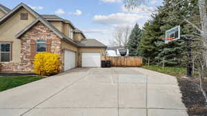 View of side of home featuring stone siding, driveway, a garage, and stucco siding
