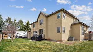 Rear view of property featuring fence, a yard, central air condition unit, and stucco siding