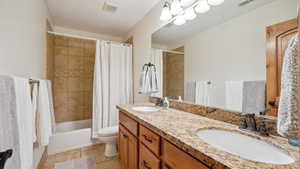 Bathroom with double vanity, toilet, shower / bath combo, and a sink