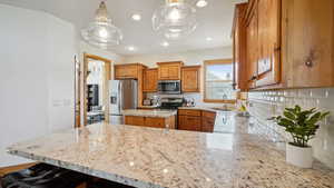 Kitchen with a sink, decorative backsplash, brown cabinets, light stone counters, and appliances with stainless steel finishes