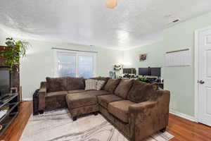Living room featuring visible vents, a textured ceiling, baseboards, and wood finished floors
