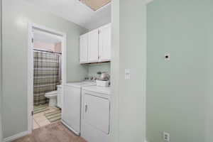 Laundry area featuring independent washer and dryer, light carpet, light tile patterned flooring, and cabinet space