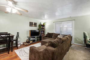 Living area featuring ceiling fan, baseboards, wood finished floors, and a textured ceiling