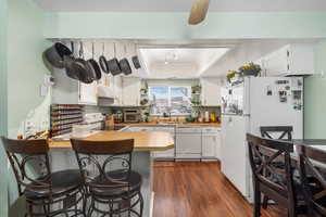 Kitchen with white appliances, dark wood-style floors, a peninsula, under cabinet range hood, and a tray ceiling