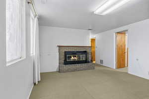 Unfurnished living room featuring a brick fireplace, baseboards, visible vents, and carpet