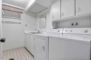 Clothes washing area with washer and dryer, light tile patterned floors, a sink, and cabinet space