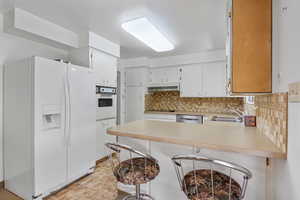 Kitchen with a peninsula, white appliances, light countertops, under cabinet range hood, and tasteful backsplash