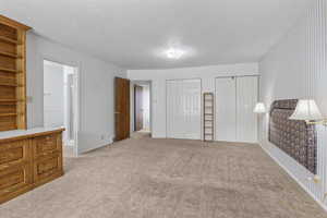 Unfurnished bedroom with connected bathroom, multiple closets, and light carpet