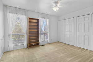 Unfurnished bedroom with carpet floors, ceiling fan, two closets, and visible vents