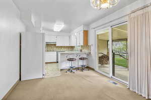 Kitchen featuring light colored carpet, an inviting chandelier, freestanding refrigerator, a peninsula, and visible vents