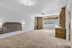 Unfurnished living room with a wood stove, a textured ceiling, ceiling fan, and carpet flooring