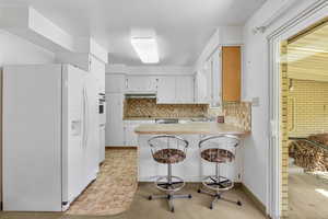 Kitchen with a peninsula, white appliances, under cabinet range hood, a sink, and backsplash