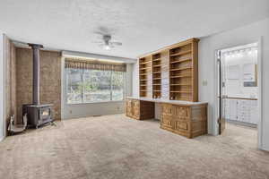 Unfurnished office featuring ceiling fan, a wood stove, a textured ceiling, and light colored carpet
