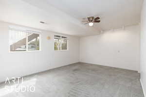 Carpeted spare room featuring rail lighting, baseboards, a ceiling fan, and visible vents