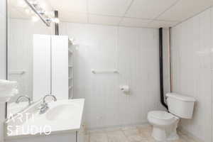 Bathroom with tile walls, toilet, vanity, and a drop ceiling