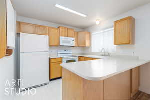 Kitchen featuring a peninsula, a sink, white appliances, light floors, and light countertops