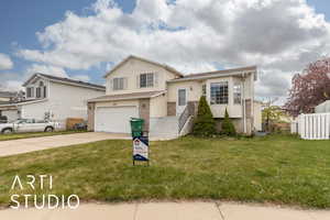 View of front of home featuring driveway, fence, a garage, brick siding, and a front yard
