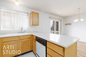Kitchen with white dishwasher, a sink, light countertops, a peninsula, and a notable chandelier