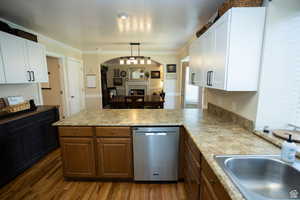 Kitchen featuring a peninsula, arched walkways, white cabinetry, dishwasher, and dark wood-type flooring