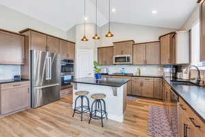Kitchen featuring dark countertops, a sink, a breakfast bar, stainless steel appliances, and a kitchen island